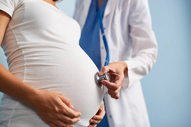 Doctor listening breath of baby in pregnant female abdomen